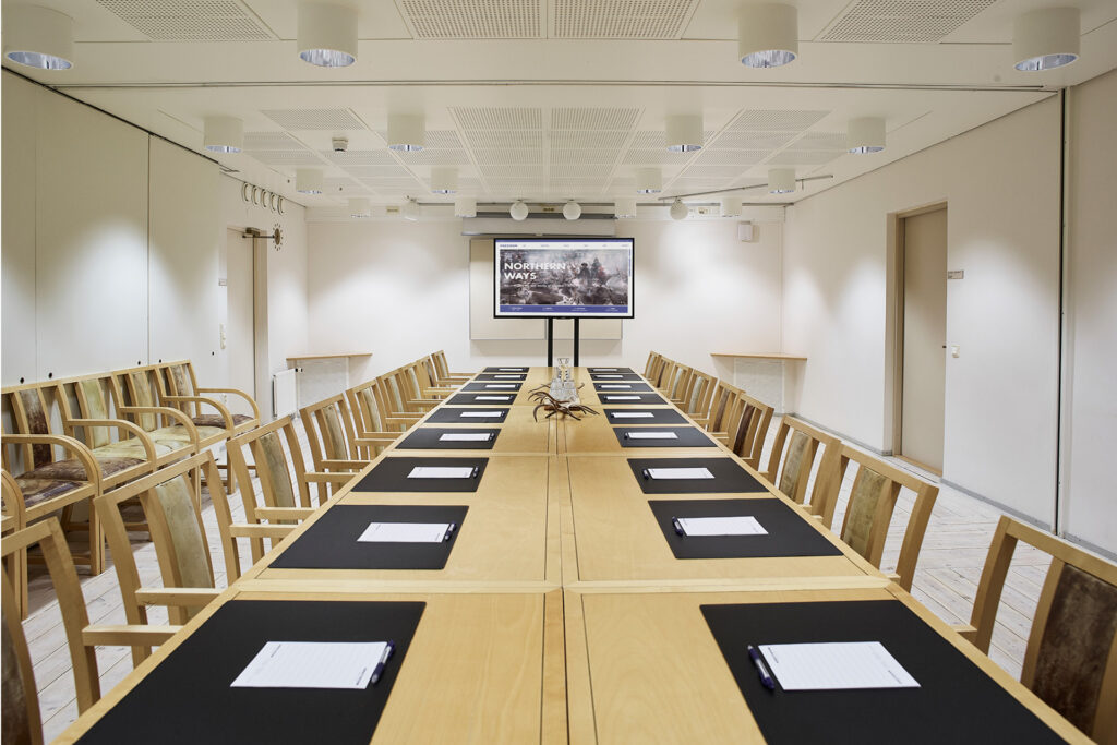 Kieppi-kokoustilassa näyttö ja pitkät pöydät vastatusten